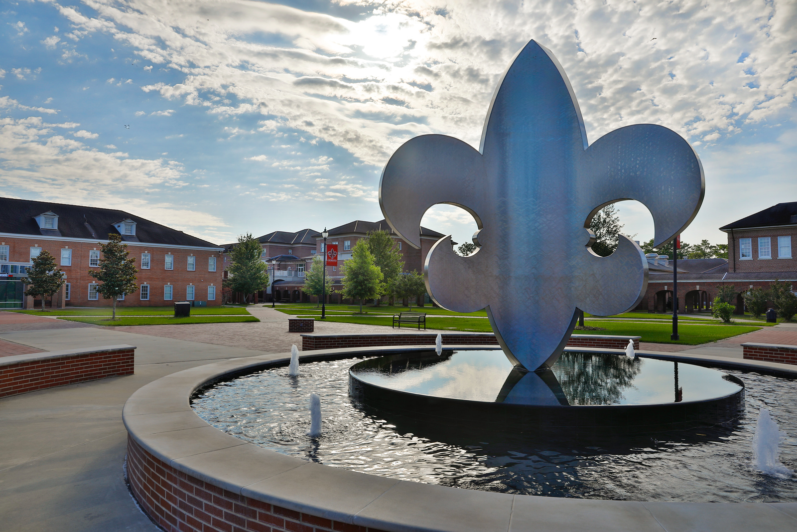 Silver fleur-de-lis fountain sits in the middle of the campus quad. In the distance are halls F.G. Mouton Hall, Moody Hall, and Lee Hall from left to right